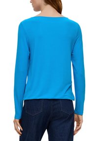 Długi rękaw w jasnoniebieskim kolorze, okrągły dekolt, wykonany z gładkiego, lekkiego materiału. Widok z tyłu pokazuje luźny krój i dłuższy dół.