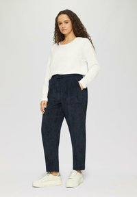 Navyblauwe, gestructureerde broek met een elastische tailleband en een trekkoord. Gecombineerd met een wit langharig top en lichte sneakers.