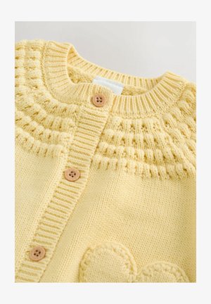 Gai dzeltens adīts kardigāns ar ribotām malām, ar rakstainu jostu, trim koka pogām un noapaļotu, izcilu sirds detaļu.