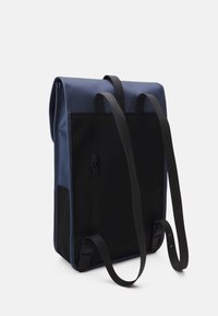 Zaino realizzato in tessuto blu e nero resistente, con spallacci neri regolabili e una tasca con zip per lo stoccaggio. Forma rettangolare.