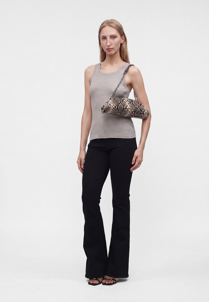 Femme portant un haut gris sans manches, un pantalon noir évasé, des talons noirs à bouts ouverts, tenant un sac à main à motif peau de serpent sur l'épaule.