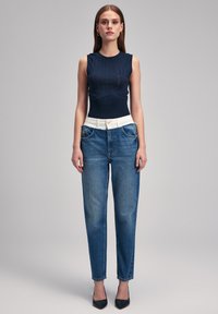 Top sin mangas de color navy con patrón texturizado, combinado con jeans de tiro alto en azul claro que presentan una cintura blanca y sutiles detalles desgastados.