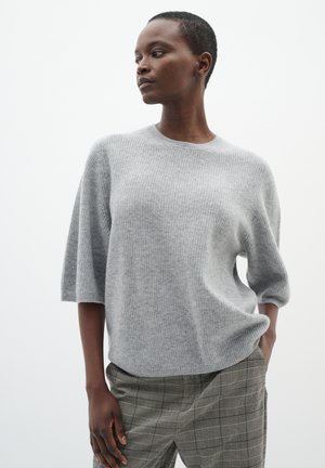 Pull en maille côtelée, gris clair, à coupe décontractée et manches larges, associé à un pantalon gris à motifs. Texture lisse ; design simple et moderne.