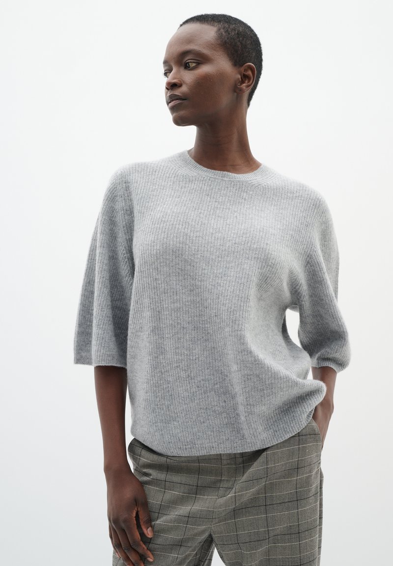 Hellgrauer, gerippter Strickpullover mit entspannter Passform und weiten Ärmeln, kombiniert mit grauen gemusterten Hosen. Glatte Textur; schlichtes, modernes Design.