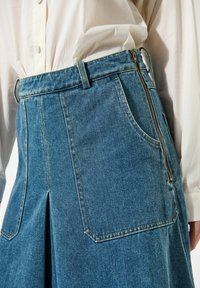 Denimska krila v modri barvi z visokim pasom, zadrgo, stranskimi žepi in sprednjim razporkom. Ima kontrastne šive.