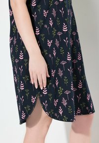 Abito navy con un motivo floreale in rosa e verde, realizzato in tessuto morbido, con spacchi laterali e maniche corte. Mano appoggiata sul tessuto.