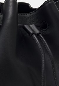 Black leather handbag with a textured surface, featuring a drawstring closure and stitched accents. Smooth material with a sleek design.