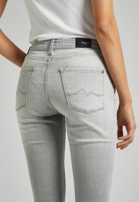 Jeans de mezclilla gris claro con un diseño ajustado, que cuentan con dos bolsillos traseros, sutiles detalles de costura y una etiqueta cerca de la cintura.