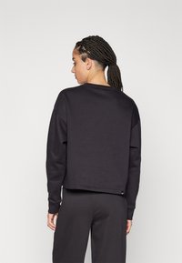 Felpa nera corta con collo rotondo, maniche lunghe e una consistenza liscia. Presenta un dettaglio del logo sull'orlo. Sono visibili pantaloni abbinati.