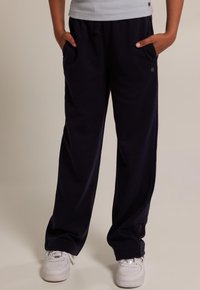 Marineblau, lockere Sweatpants aus weichem Stoff, mit Seitentaschen und elastischem Bund, kombiniert mit weißen Sneakers.