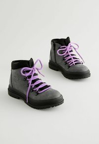 Bottes en daim grises avec des accents noirs, dotées de lacets rayés violets et blancs, et d'une semelle en caoutchouc noir robuste. Détail de fermeture éclair sur le côté inclus.