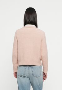 Maglione rosa chiaro, strutturato, con design crop, scollatura rotonda e maniche lunghe, abbinato a jeans in denim blu.