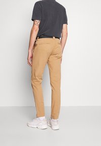 Beżowe chinosy o dopasowanym kroju, z tylnymi kieszeniami i gładką fakturą. Połączone z białymi sneakersami i ciemnoszarym t-shirtem.
