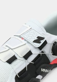 White athletic shoe with textured mesh upper, black and red accents, elastic laces, and reflective detailing on the side.
