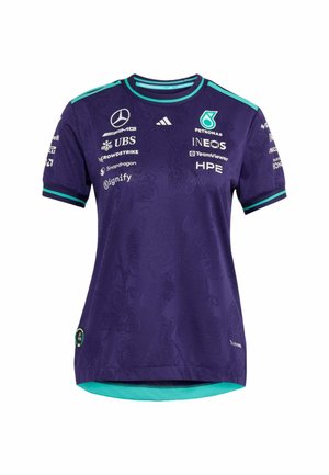 Persona che indossa una maglietta viola della squadra Mercedes AMG Petronas di Formula 1 con loghi degli sponsor e strisce turchesi sulla spalla.