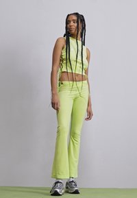 Neon green crop top and flared pants made of stretchy fabric, featuring side ties on the top. Model wears black and white sneakers.