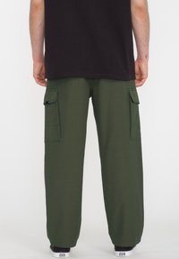Groene cargobroek van katoen met een losse pasvorm, voorzien van zijzakken en een cuffed zoom. Draagt met een zwart T-shirt en sneakers.