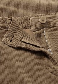 Manšestrové kalhoty v světle hnědé barvě, s měděným zipem, knoflíkovým zapínáním a texturovanou ribbenou tkaninou. Viditelné podrobné švy.