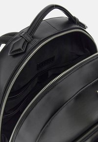 Intérieur d'un sac à dos en cuir noir avec une fermeture éclair, plusieurs poches et une doublure lisse et texturée.