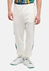Witte sweatpants met zijpatronen in blauw, oranje en geel, met een tapered fit en ribgebreide enkelmanchetten, gecombineerd met witte sneakers.