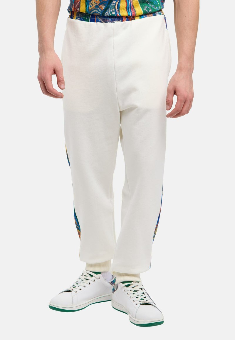 Witte sweatpants met zijpatronen in blauw, oranje en geel, met een tapered fit en ribgebreide enkelmanchetten, gecombineerd met witte sneakers.