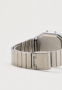 Nerūdijančio plieno laikrodis su aštuonkampiu korpusu, matinėmis ir blizgiomis apdailomis, sujungta apyrankė ir sagtis su žyma "CASIO."