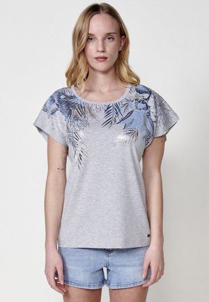 Camiseta gris de manga corta con un estampado floral azul en los hombros y un corte relajado. Textura suave, cuello redondo y diseño minimalista.