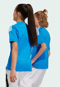 Blå idrottströjor med korta ärmar, prydda med vita tri-stripes på axlarna och ett texturerat mönster på baksidan. Vita byxor.