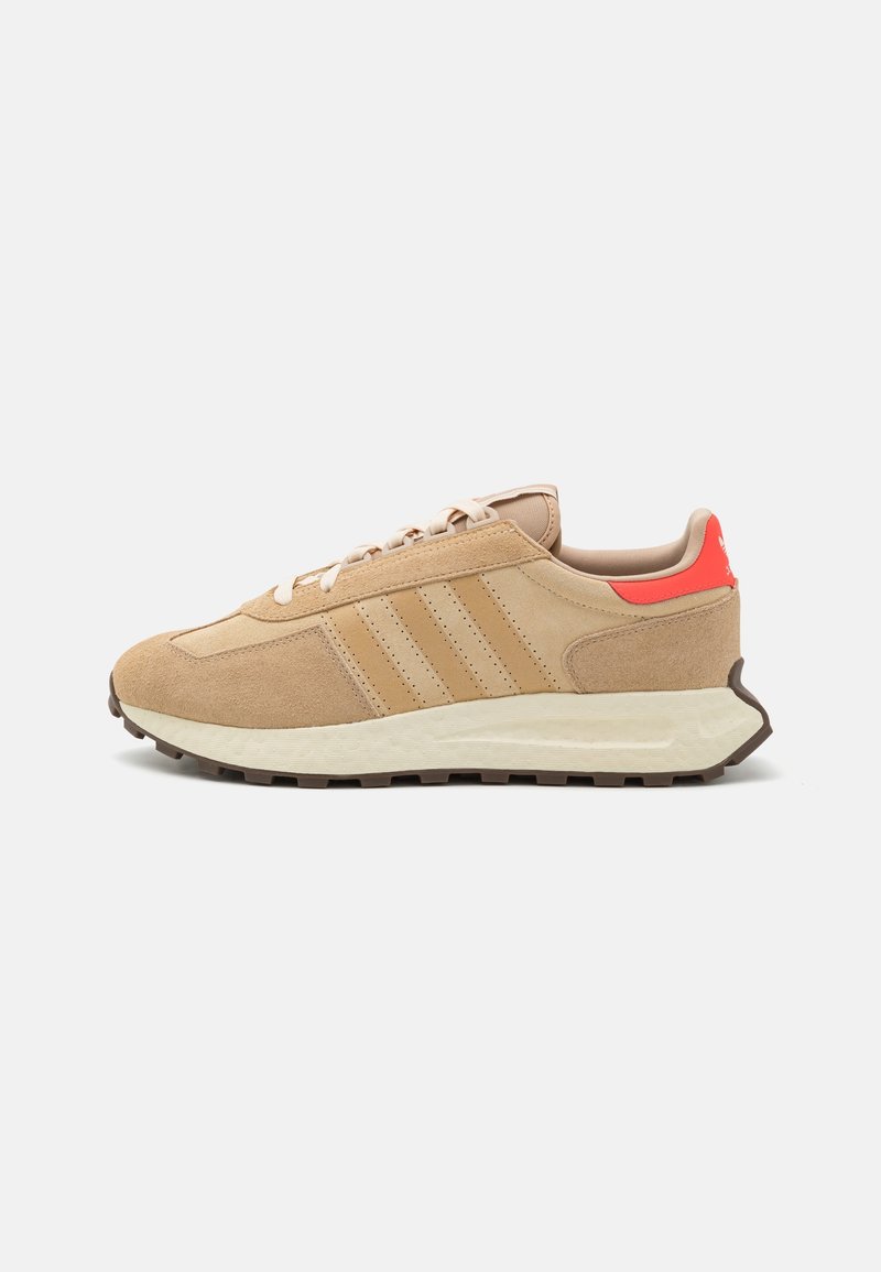 Beige suede sneakers with three beige stripes, a textured cream sole, and a bright orange accent at the heel. Classic running shoe silhouette.