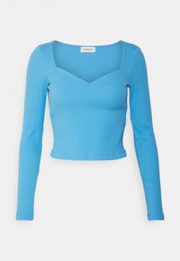 Långärmad, figurnära topp i ljusblå ribbad tyg, med fyrkantig utskärning och kortad fåll. Slät textur utan mönster eller accent.