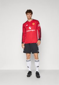 Piros, hosszú ujjú mez Manchester United logóval, fekete rövidnadrág, fehér zoknik fekete csíkokkal, és fekete focicipők.