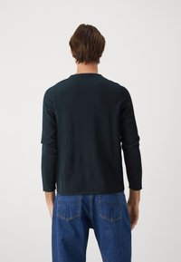 Czarna bluzka z długim rękawem, wykonana z miękkiego materiału, z okrągłym dekoltem i luźnym krojem. Tylny widok ukazuje prosty design bez ozdób.