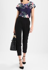 Marinblå topp med blommönster och korta ärmar, matchad med svarta capribyxor och svarta klackskor med ankelrem, bärande på en svart handväska.