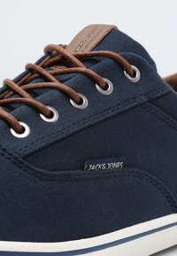 Námořnické plátěné tenisky s hnědými koženými tkaničkami a očky, bílé gumové podrážky, s malou modrou etiketou označenou "JACK & JONES".