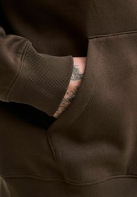 Brown hoodie featuring a ribbed cuff and kangaroo pocket, with a smooth texture and visible stitching details.