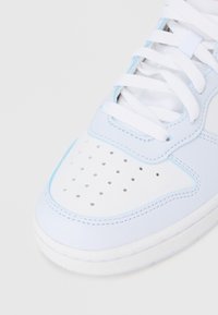 Λευκό και ανοιχτό μπλε αθλητικό παπούτσι με δερμάτινη και διάτρητη περιοχή στα δάχτυλα. Λευκά επίπεδα κορδόνια και μπλε λεπτομέρειες κατά μήκος των ραφών. Λαστιχένια σόλα.