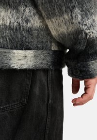 Wollmischungsjacke in Dunkelgrau mit hellgrauen und weißen Streifen, mit einem geknöpften Ärmelbündchen und einem weichen, strukturierten Finish. Schwarze Denim-Hose sichtbar.