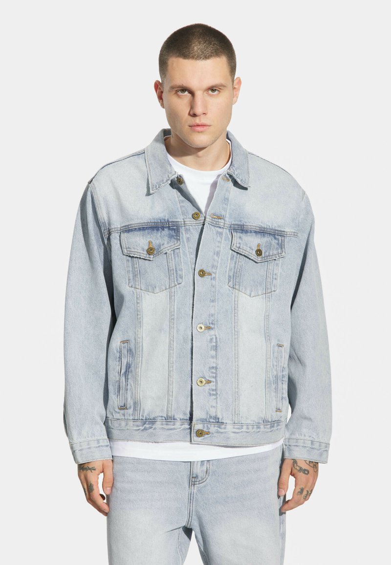 Jasnoniebieska dżinsowa kurtka o luźnym kroju, z dwoma kieszeniami na piersi, zapięciem na guziki i minimalnymi przetarciami.