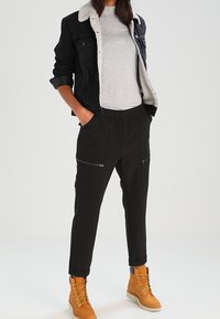 Svart denimjacka med fårskinnskrage, grå t-shirt, svarta joggerbyxor med dragkedjefickor och tanfärgade snörkängor.