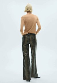 Beige aansluitend shirt met lange mouwen, gecombineerd met hoge taille flared broeken van nepleer met een slangenpatroon in donker groen en zwart.
