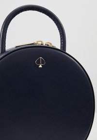 Borsa a mano rotonda in pelle navy con manico testurizzato e hardware dorato, dotata di un piccolo logo a forma di paletto sul davanti.