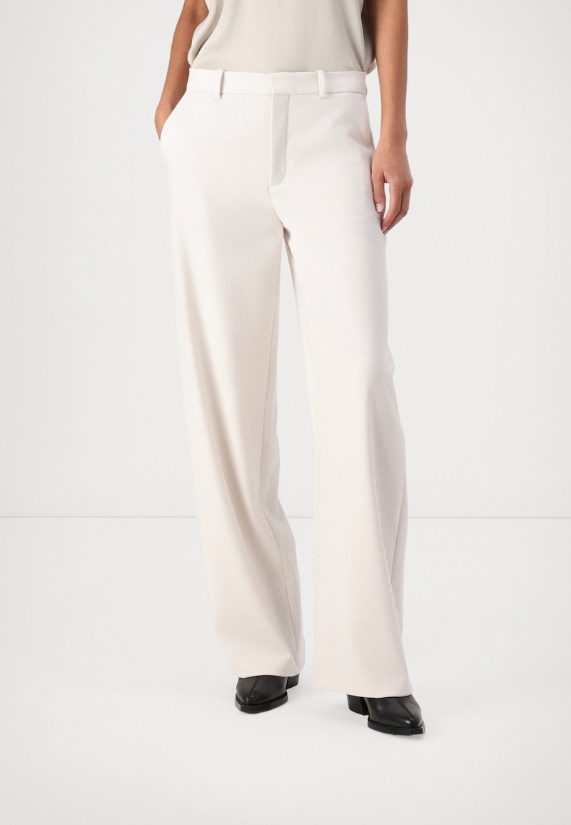 Witte wijde broek met een gladde textuur, met een vlakke voorkant, riemlussen en zijzakken, gecombineerd met zwarte schoenen.