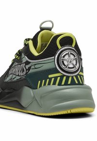 Baskets noires et grises avec des accents verts. Présentent un logo en forme de roue au niveau du talon, des panneaux texturés et des éléments réfléchissants dans le design.