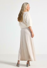 Lys beige striktrøje med korte ærmer, parret med en lang, flydende crèmefarvet nederdel. Grå blokhælede sandaler fuldender outfittet.