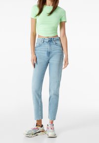 Ljust grön kortärmad t-shirt, högmidjade ljusblå jeans med slitna detaljer, och flerfärgade sneakers med djärva accenter.