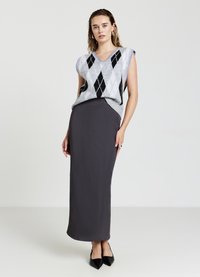 Maglione senza maniche grigio con motivo a rombi in bianco e nero, abbinato a una gonna lunga aderente grigio scuro e scarpe nero con punta.