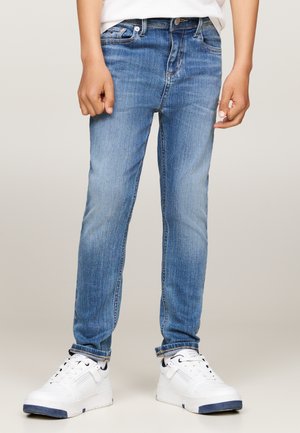 Jeans in denim blu con vestibilità slim e leggera scoloritura, abbinati a sneakers bianche con accenti blu navy e suola testurizzata.