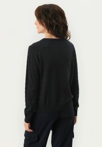 Pulover negru tricotat cu guler rotund, man�șete și tiv ribbate. Designul are o textură netedă și o croială lejeră.
