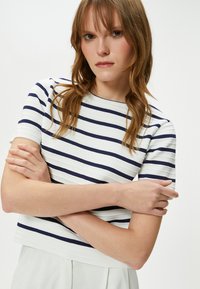 Stribet kortærmet top i hvid og marineblå, med ribbet tekstur og en rund halsudskæring. Bunden er cropped med vandrette striber.