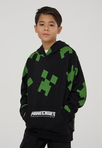 Felpa nera con cappuccio caratterizzata da motivi verdi pixelati, tasca frontale e logo "Minecraft". Tessuto morbido con vestibilità comoda e cappuccio.